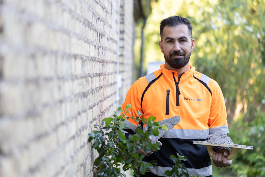 Håndværker fra ServicePlus arbejder på facaderenovering ved en murstensbygning.